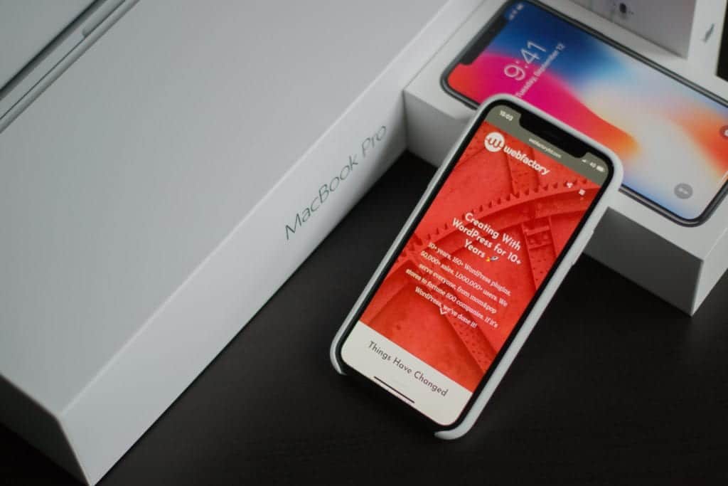iPhone X next to a MacBook Pro and iPhone packaging showing a WordPress website