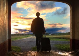 Man pulling luggage walking near gray concrete road during sunset