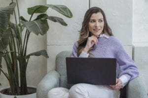 Positive young woman working on netbook sitting in armchair in office