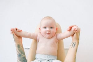 Unrecognizable woman holding baby by hands on knees in light bedroom