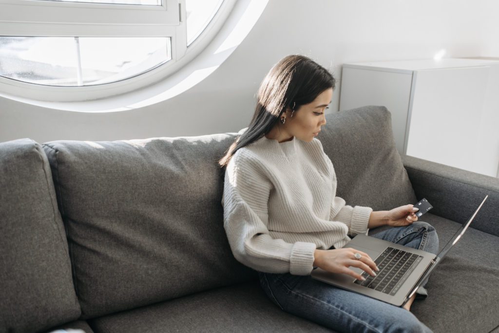 Woman in white sweater sitting on couch using laptop