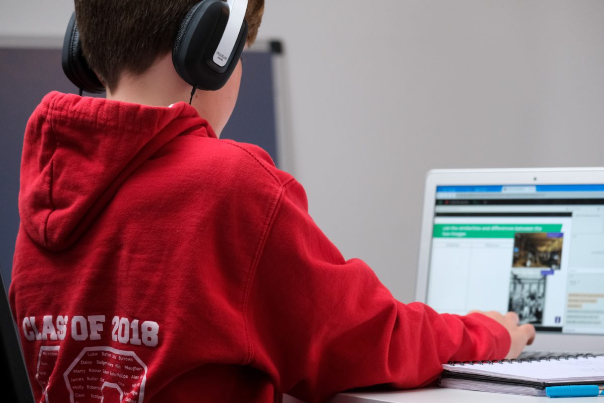 Home schooling during lockdown, boy working on school work with laptop and headphones during coronavirus covid 19 lock down. Remote learning through home schooling due to school closures has become commonplace in the UK in 2021.