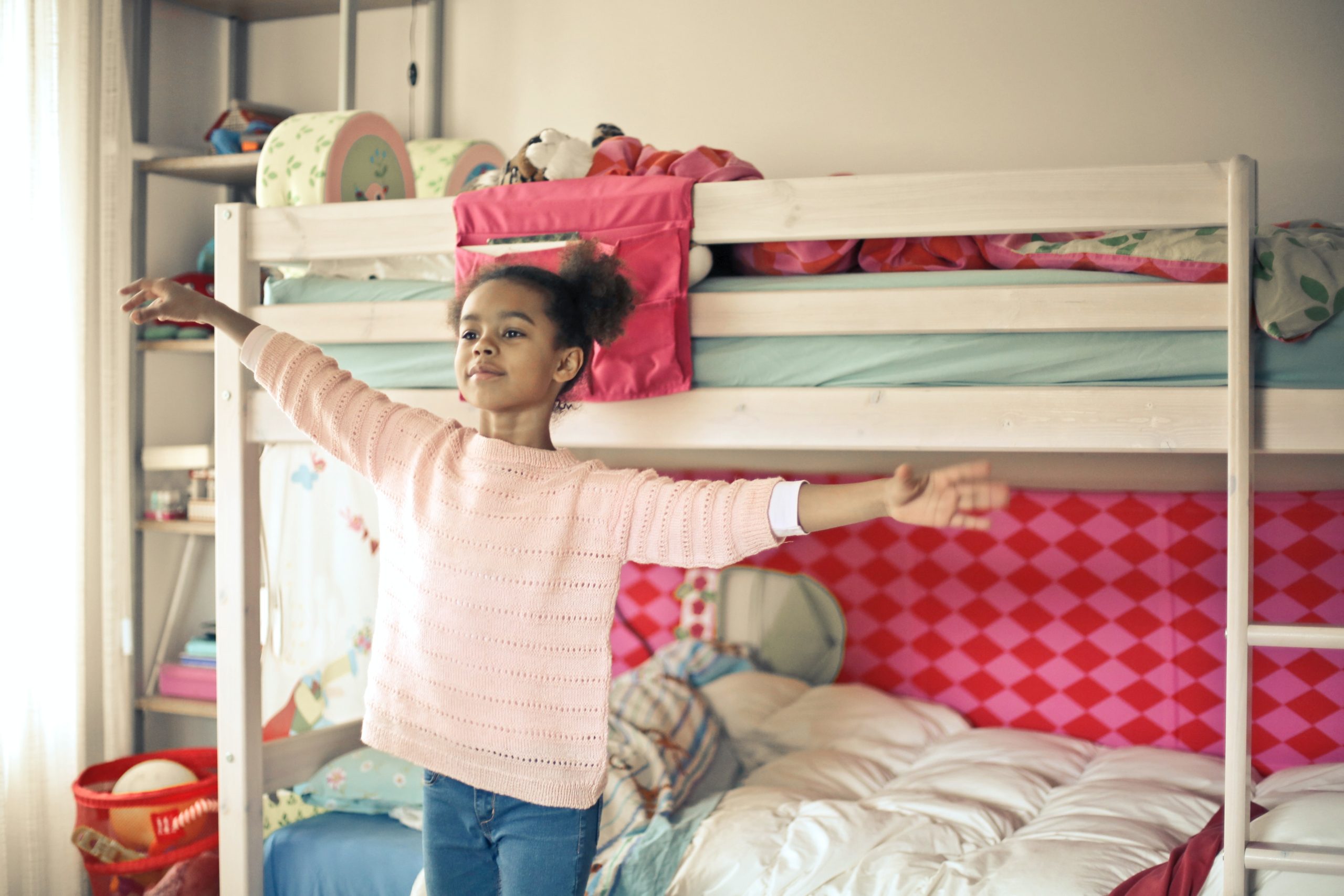 A girl standing in front of a bunk bed, with her hands in the air.