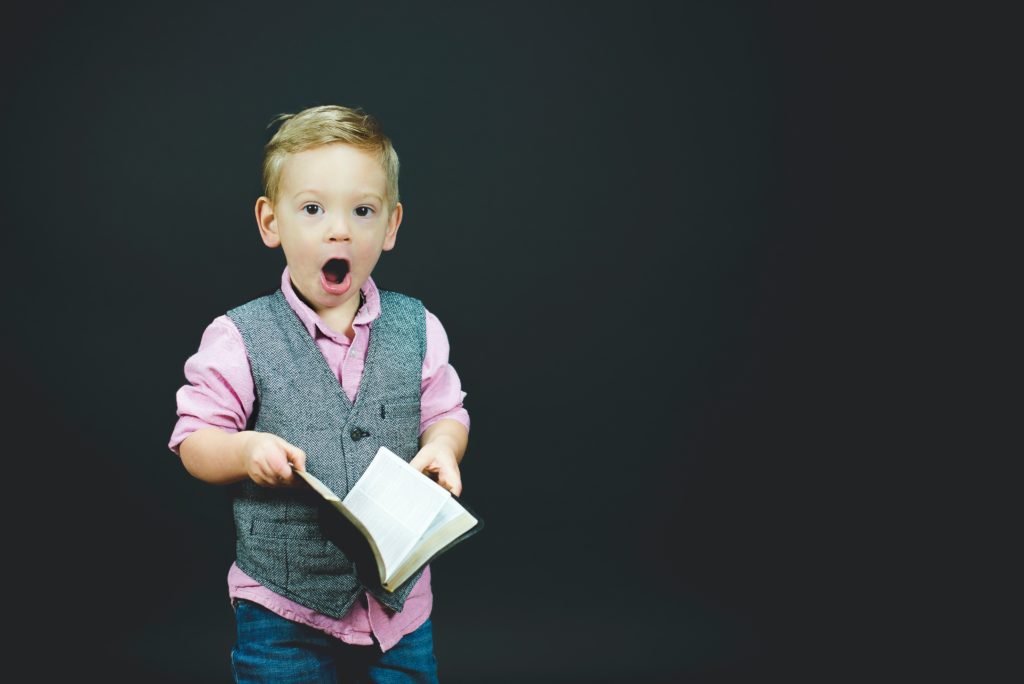 A kid holding a book, with his mouth open